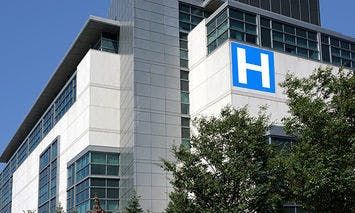 A modern hospital building exterior displays a large blue 
